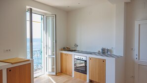 A modern kitchen with a large window, wooden cabinets, a built-in oven, and a marble countertop. - Newly Renovated Ocean View Flat (Sori)