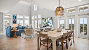 Un salón comedor amplio con una mesa grande, asientos cómodos, televisor y ventanas amplias que ofrecen vistas al exterior.