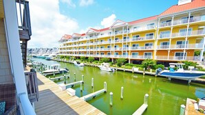 Un port de plaisance avec des bateaux amarrés, une terrasse en bois et un hôtel doté de nombreux balcons et d’un toit rouge.