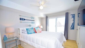 Une chambre à coucher avec un lit, une table de chevet, un ventilateur de plafond et une fenêtre avec des rideaux.