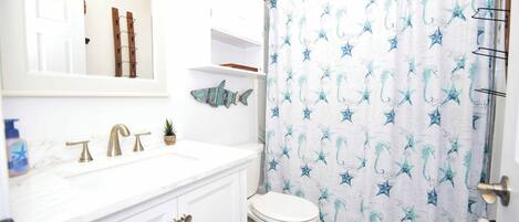 Un baño con un lavabo blanco, dos grifos dorados, un inodoro blanco y una cortina de ducha con motivos de estrellas de mar y caballitos de mar.