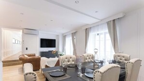 Un comedor con una mesa negra, sillas tapizadas en color beige y un televisor de pantalla plana montado en la pared.