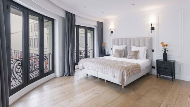 Un dormitorio moderno con una cama grande, una mesita de noche y vistas a la ciudad a través de amplios ventanales.