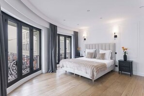 A modern bedroom with a large bed, a nightstand, and a view of the city through large windows.
