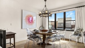 A dining room with a round table, clear chairs, and a chandelier.