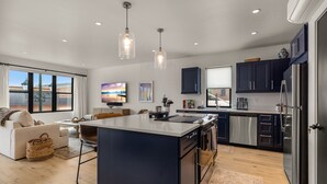 A modern kitchen with a central island, dark cabinetry, stainless steel appliances, and pendant lighting.