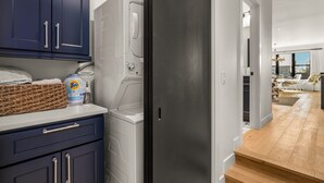 A laundry room with a washing machine, a basket, and a Tide detergent bottle.