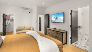 A modern bedroom with a large bed, a TV mounted on the wall, a wardrobe, and a door leading to another room.