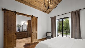 Ein Schlafzimmer mit einem großen Bett, Holztüren, die sich verschieben lassen, einer Chandelierleuchtre und Blick ins Freie.