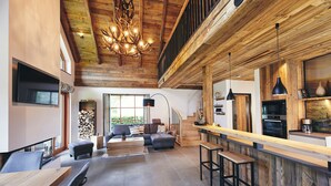 A spacious living area with a high ceiling, a fireplace, a dining area, and a kitchen with modern appliances. - Atempause Sauerland feel-good chalet "Große Sehnsucht" (Schmallenberg)