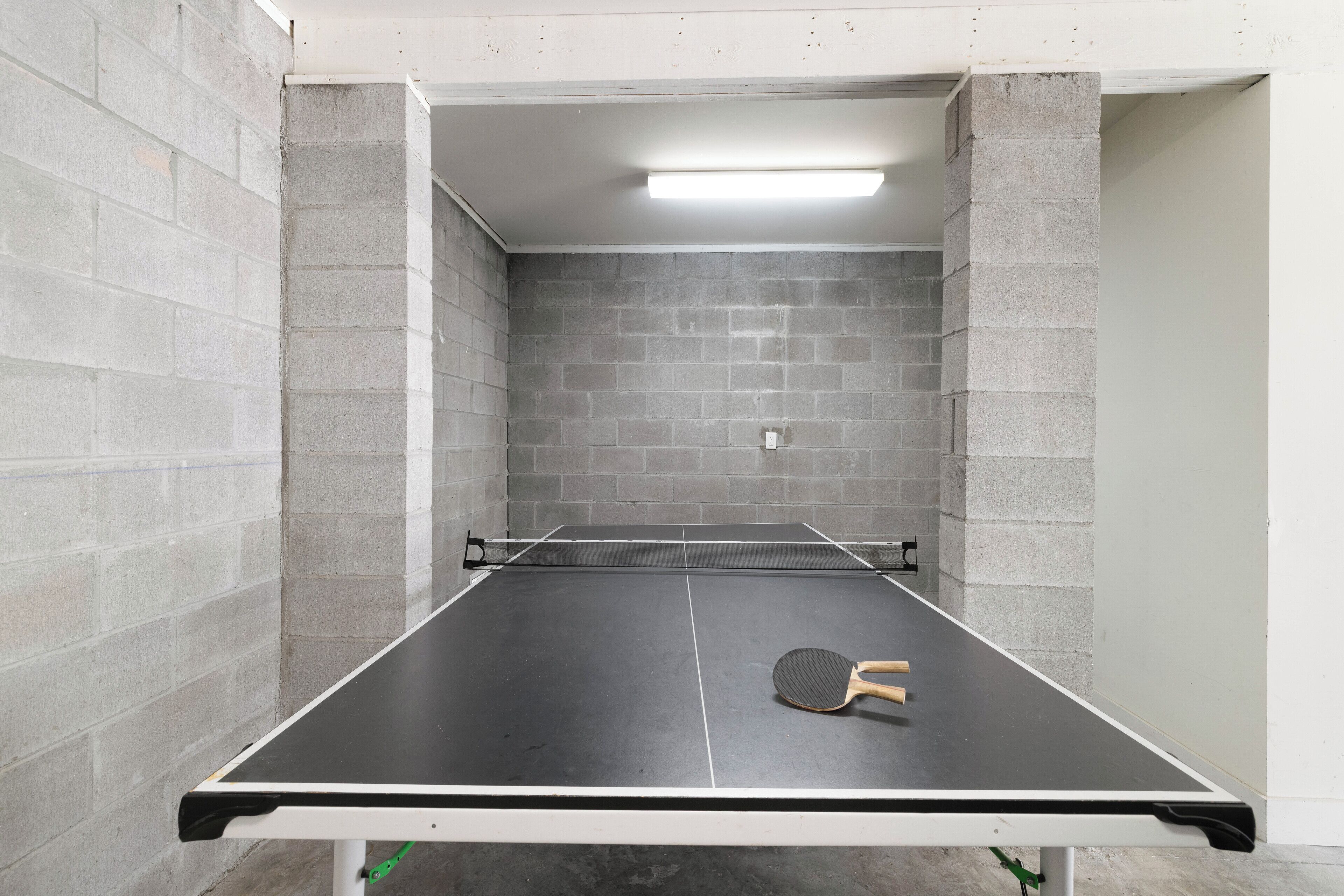 Une table de ping-pong dans une pièce aux murs en briques grises et au plafond blanc.