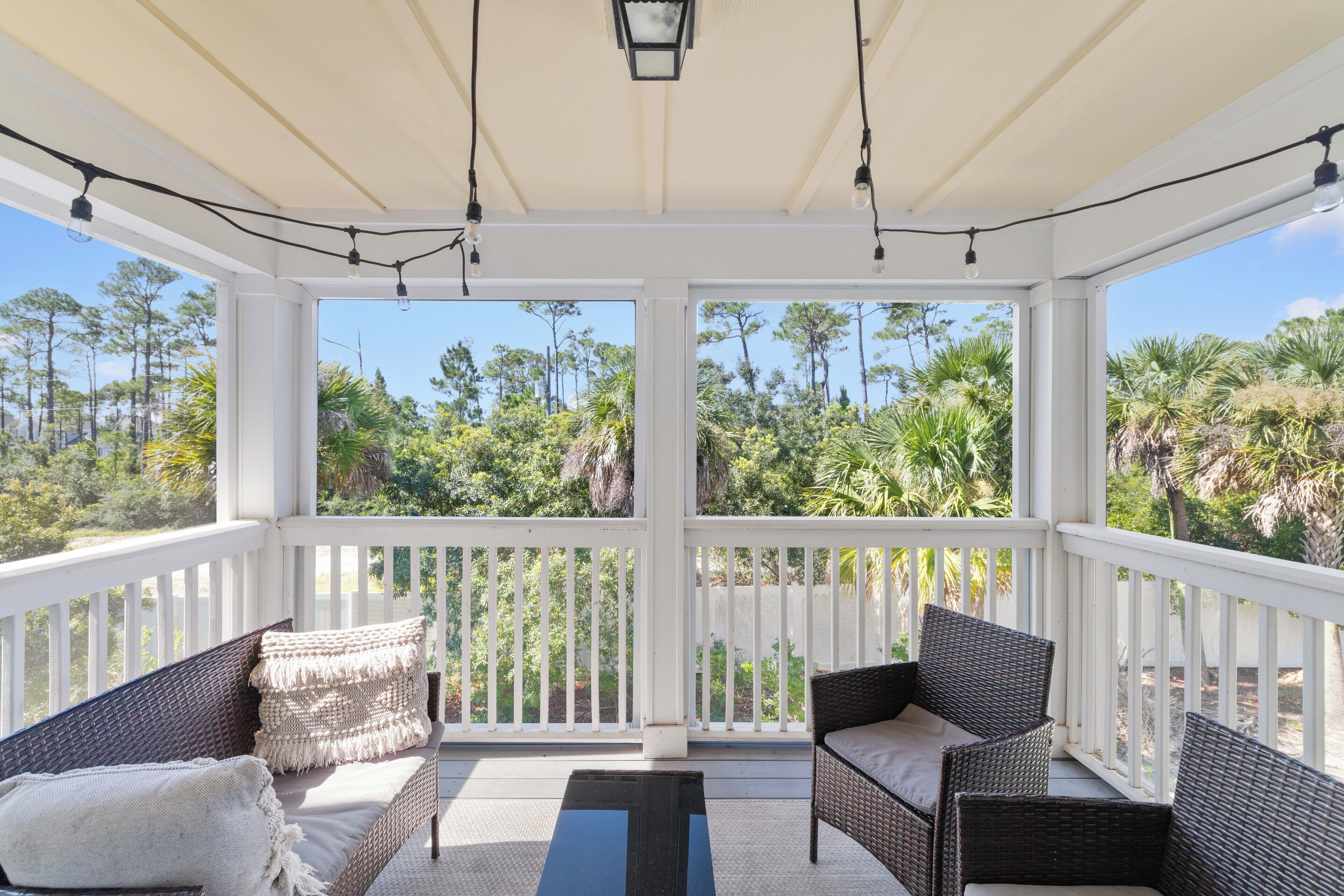 A covered outdoor seating area with wicker furniture and a view of tropical trees.