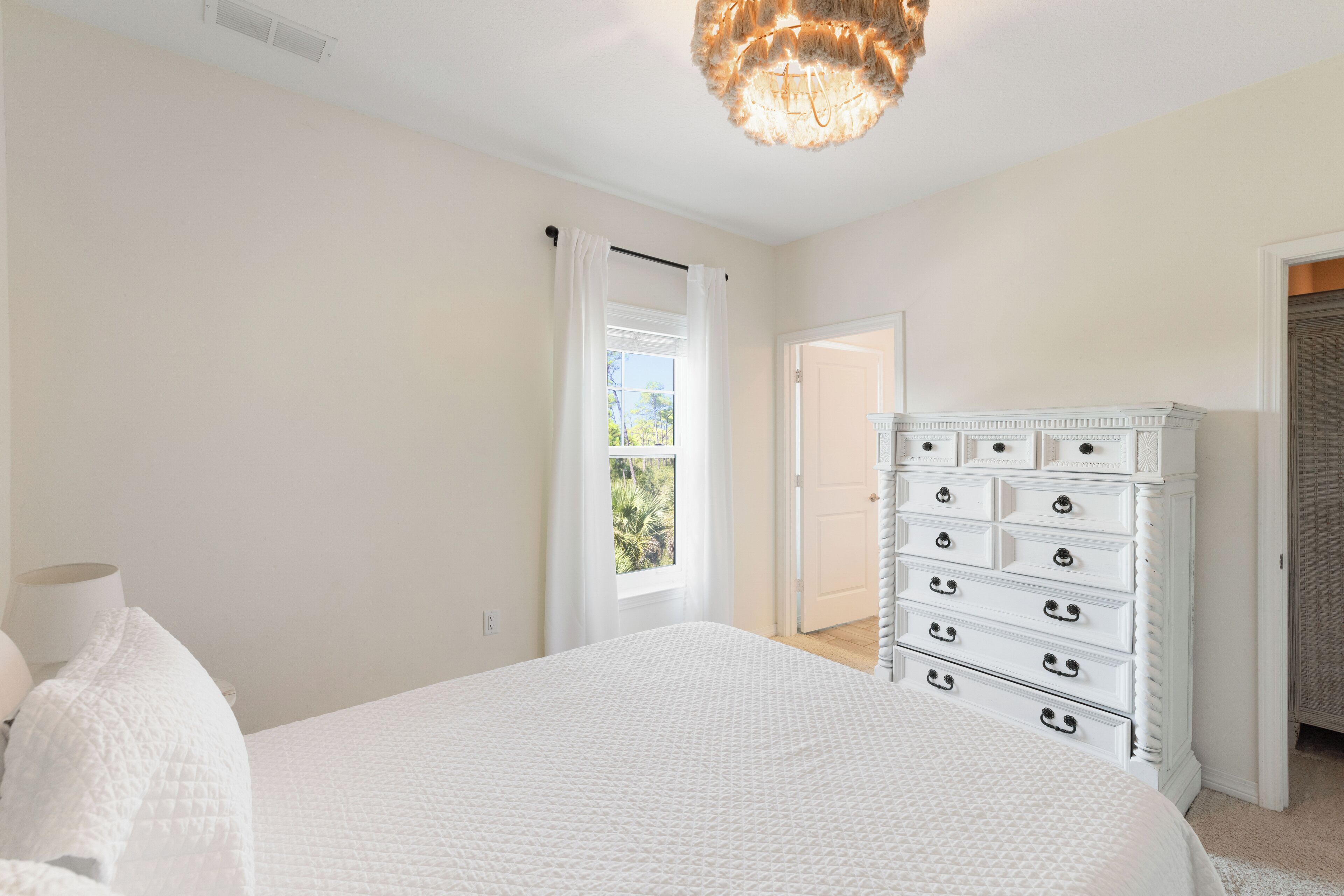 A bedroom with a large bed, a dresser, and a window with curtains.