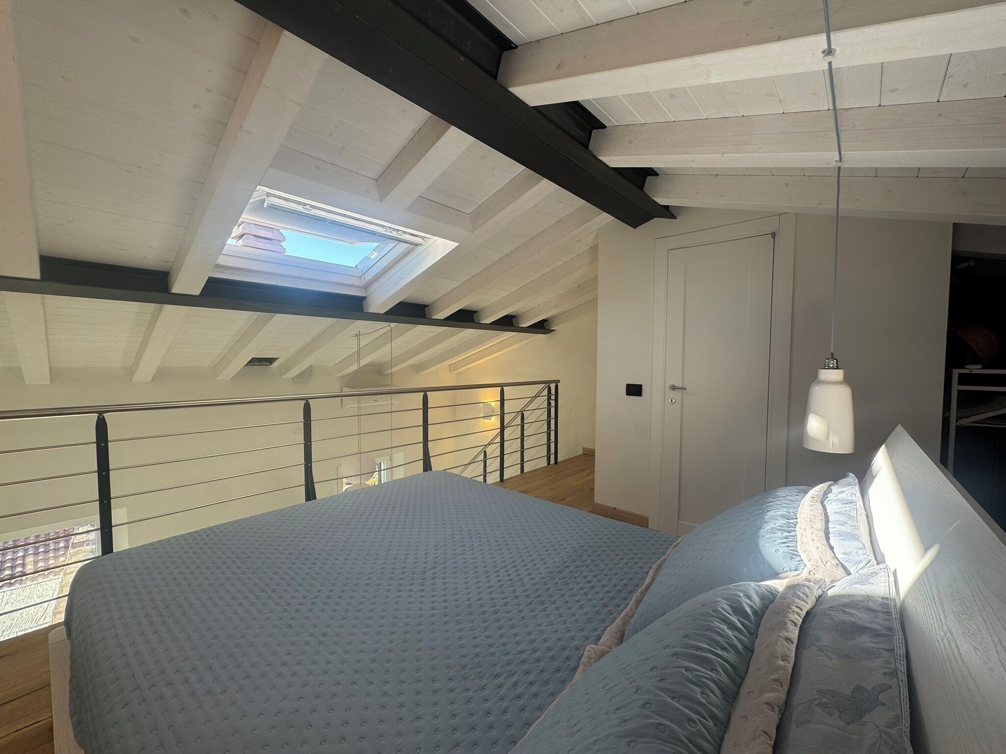 A bedroom with a large bed, a skylight, a staircase, and a hanging light fixture.
