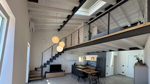 A modern interior with a staircase leading to a mezzanine, a kitchen area, and a seating area with a patterned rug. - Casina di Nonna Meca by Solturelba (Capoliveri)