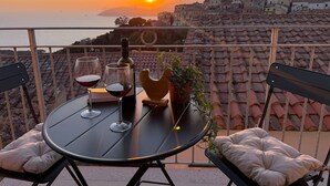 A table with two wine glasses and a bottle, a potted plant, and a view of a coastal town at sunset. - Casina di Nonna Meca by Solturelba (Capoliveri)