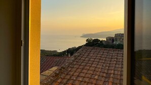 A view through a window of a coastal area with terracotta rooftops and a distant view of the sea and mountains. - Casina di Nonna Meca by Solturelba (Capoliveri)