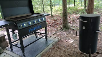 A portable barbecue grill with wheels, a gas tank, and a label reading 'EVEN EMBERS.'