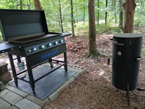 A portable barbecue grill with wheels, a gas tank, and a label reading 'EVEN EMBERS.' - TWG - Tent Campsite (1) (Graysville)