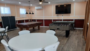 Una habitación con mesa de billar, mesa de futbolín y televisor instalado en la pared.