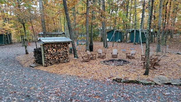 Un camping con bancos de madera, un hoyo para fuego y una pila de leña.