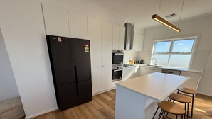A modern kitchen with white cabinetry, a black refrigerator, a central island with stools, and a window providing natural light. - Sea Escape - Sea Views!  Short walk to Tavern! Off Peak Special available! (Point Turton)