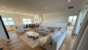 A modern living room with a sofa, coffee table, and a dining area with chairs and a table. - Sea Escape - Sea Views!  Short walk to Tavern! Off Peak Special available! (Point Turton)