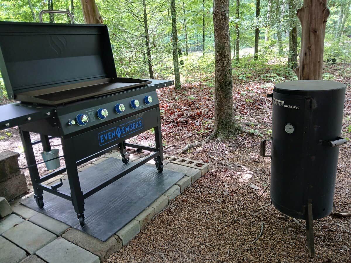 An outdoor grill setup with wheels, a portable smoker, and a metal grill pan.