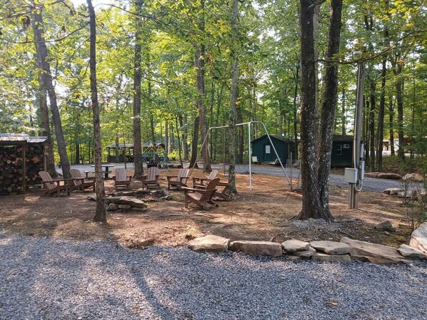 An outdoor seating area with wooden chairs and tables, surrounded by trees and gravel.