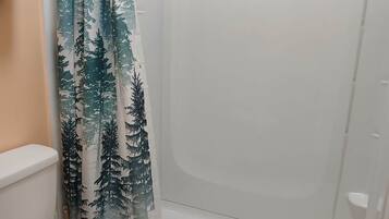 A bathroom with a toilet, a shower with a forest-themed curtain, and a green bath mat.
