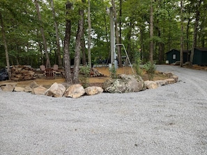 A gravel parking area with a wooden fence, trees, and a playground.