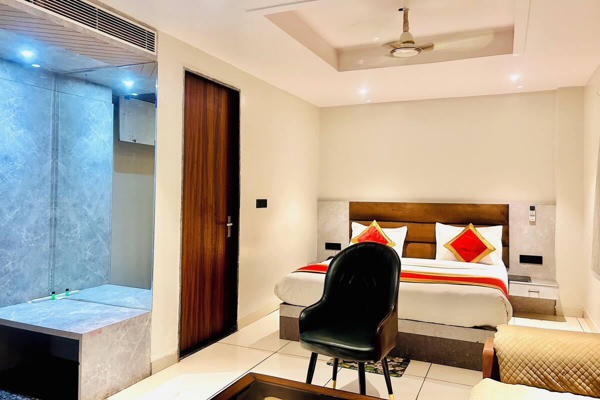 Habitación de hotel con cama, una silla, mesita de noche y zona de ducha.