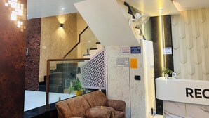 A reception area with a marble reception desk, a brown leather sofa, a staircase, and a patterned wall. - Hotel Kamakhya Inn (Chhatarpur)