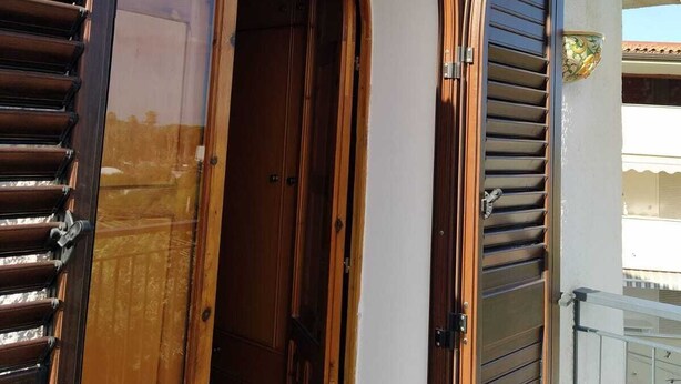 A building entrance with wooden doors and shutters, a white wall, and a metal lantern.