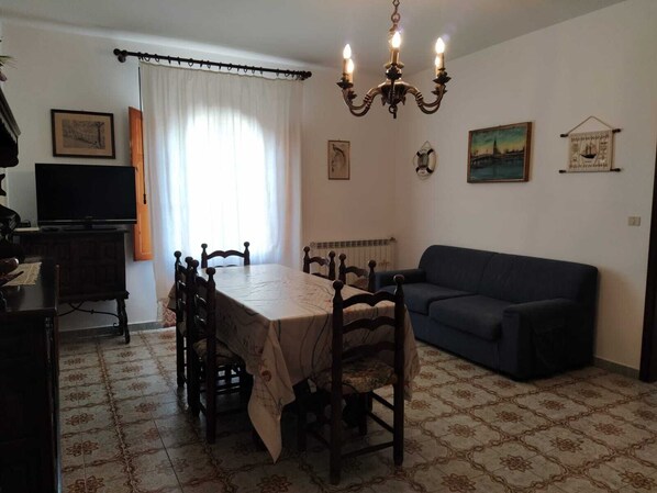 A dining area with a table and chairs, a television, a sofa, and a chandelier. - Mediterranean-style vacation home Teste di Moro (Giardini Naxos)