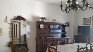 A dining room with a wooden table, chairs, a chandelier, a mirror, and a cabinet with decorative plates.