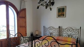 A bedroom with a bed, a wooden door, a chandelier, and a painting on the wall.