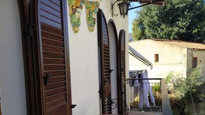 A small outdoor patio with a round table and two chairs, a wooden door, and decorative wall art.
