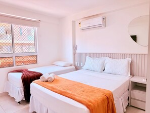 Une chambre d’hôtel avec deux lits, un appareil de climatisation, une table de chevet avec un téléphone et une fenêtre donnant sur l’extérieur.