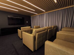 Un cine en casa con un televisor de pantalla plana, varios sofás color beige, alfombra oscura y un techo de madera con iluminación lineal.