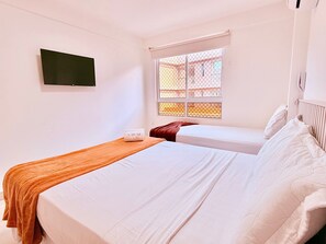 Ein Hotelzimmer mit zwei Betten, einem an der Wand befestigten Fernseher und einem Fenster mit Blick auf Gebäude.