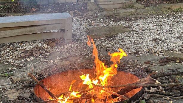 A backyard with a fire pit surrounded by rocks and logs.