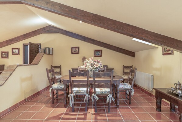 A dining area with a high ceiling, wooden beams, a dining table surrounded by chairs, and a flower vase.