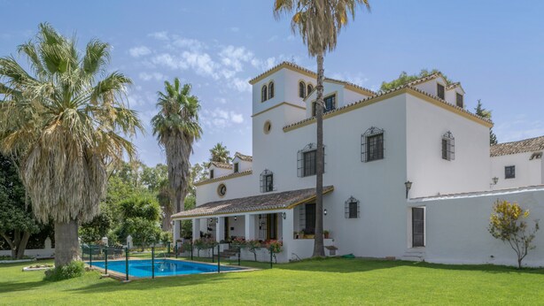 Un edificio blanco con piscina, palmeras y cielo despejado.