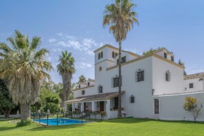 A white building with a pool, palm trees, and a clear sky.