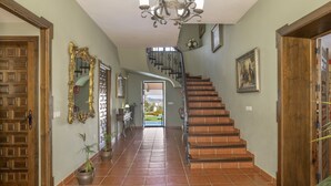 Un pasillo amplio con una escalera de madera, un candelabro y plantas en macetas.