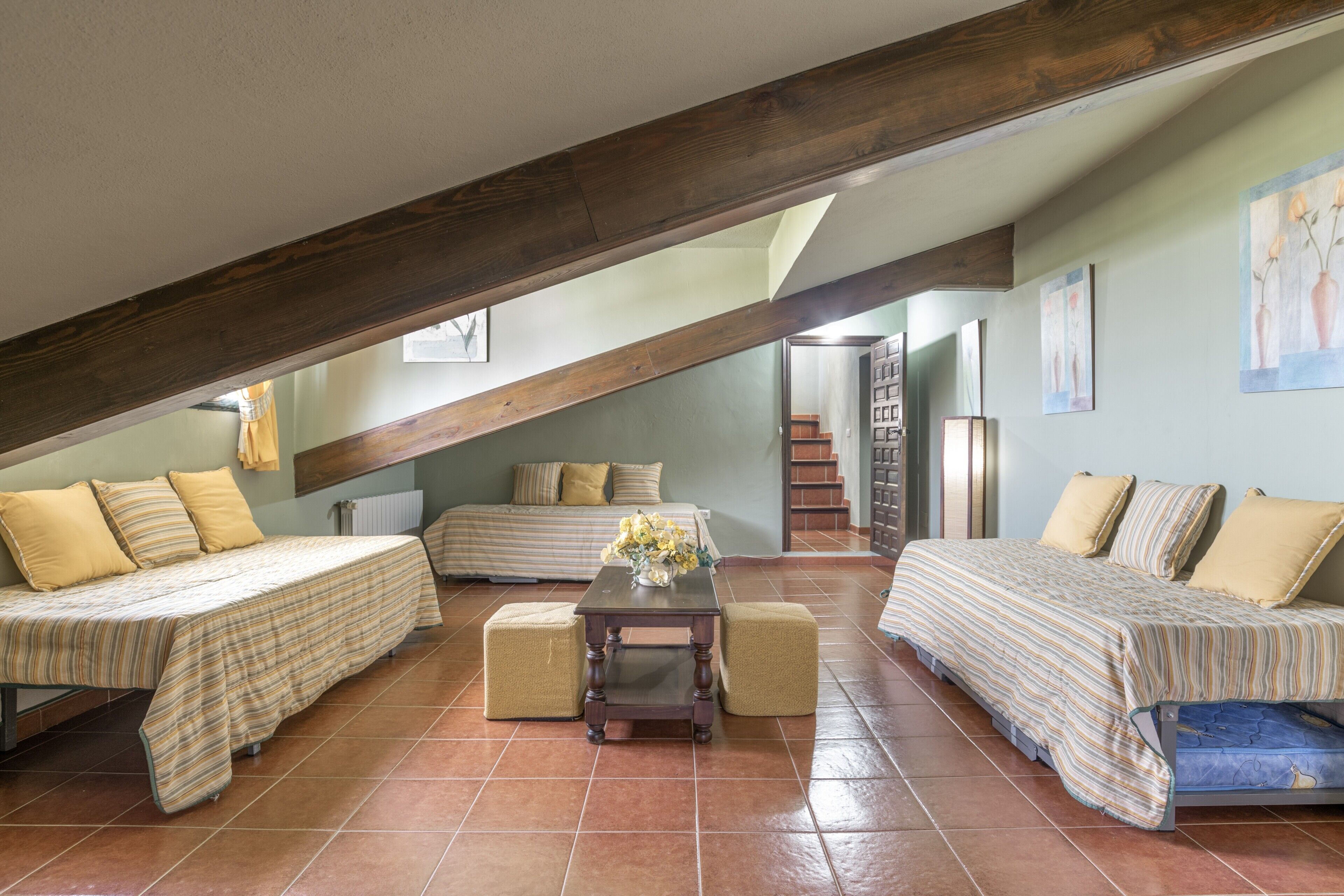 A loft bedroom with two beds, a small table, and a staircase leading to an upper level.