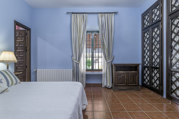 A bedroom with a bed, a window with curtains, a radiator, and a cabinet.