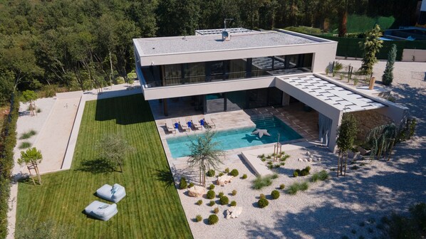 Une maison moderne à deux étages, dotée d’une piscine, d’une pelouse bien entretenue et d’un jardin agrémenté de rochers et d’arbustes.