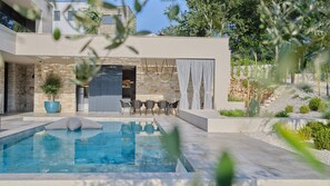 Un espace piscine extérieur moderne, avec des murs en pierre, un coin salon et une vue sur une maison contemporaine.